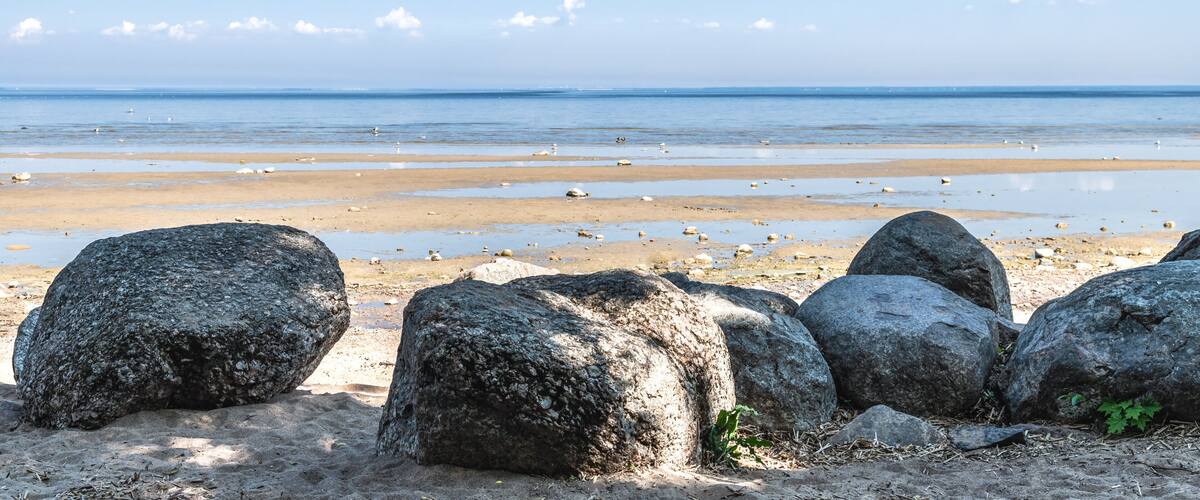 A beach with large rocks in the foreground and a calm sea under a clear sky.