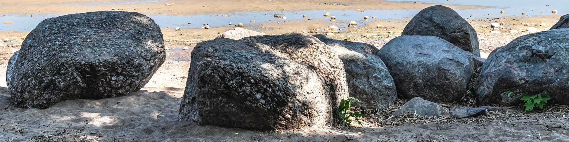 A beach with large rocks in the foreground and a calm sea under a clear sky.