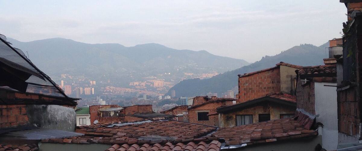 A mountainous landscape with terracotta-roofed buildings and a distant cityscape.