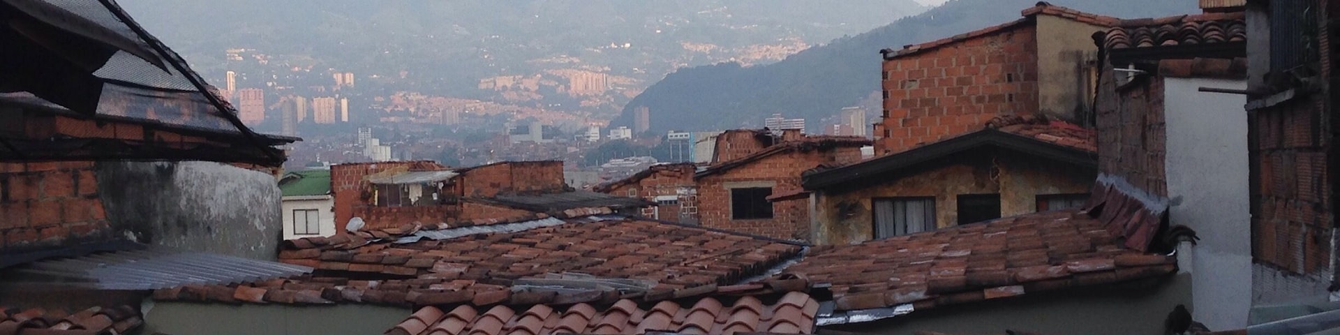 A mountainous landscape with terracotta-roofed buildings and a distant cityscape.