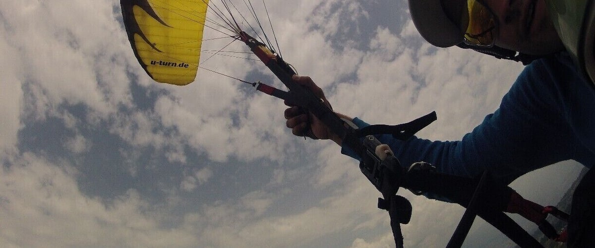 A person paragliding with a yellow canopy, wearing a helmet and sunglasses.
