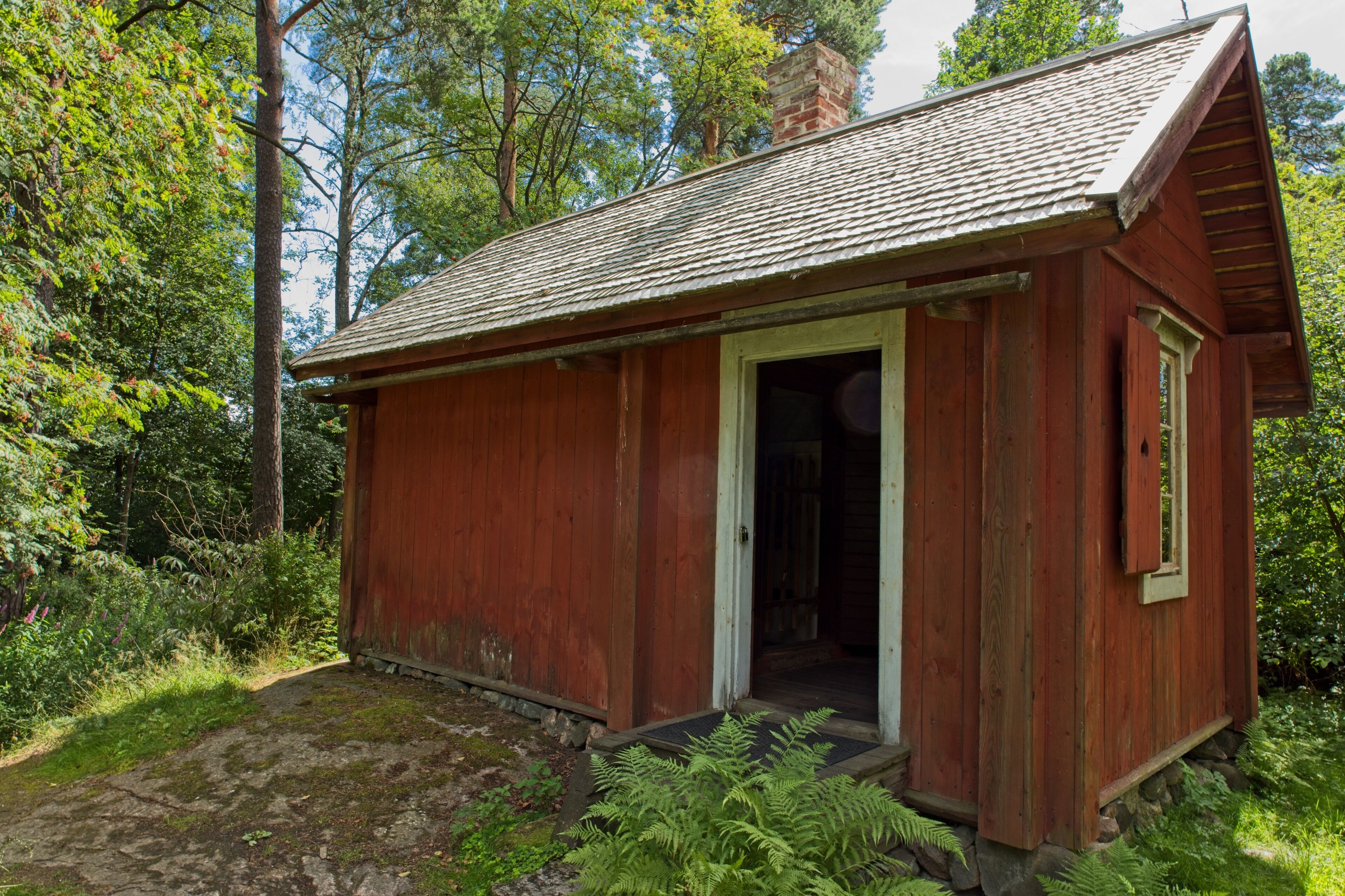 A small wooden cabin with a sloped roof surrounded by lush greenery.