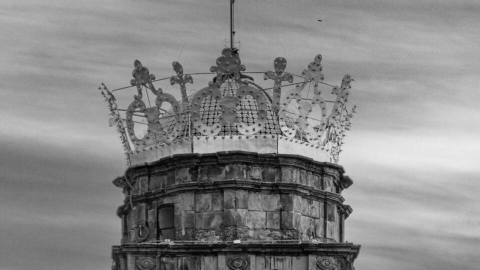A historic tower with a weather vane, bell, and ornate crown-like structure.