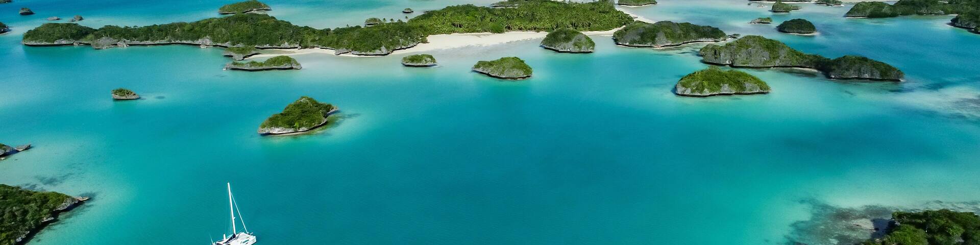 A turquoise sea with numerous small islands, a sailboat, and a distant coastline.