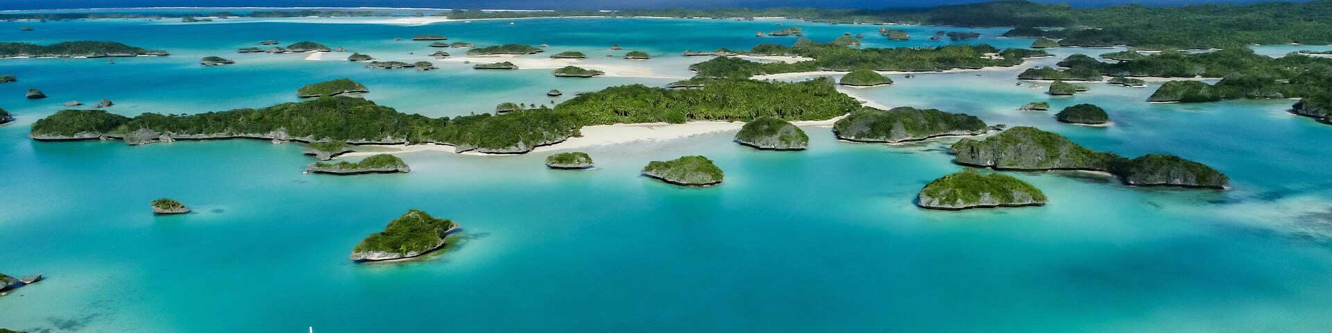 Un mar turquesa con numerosas islas pequeñas, un velero y una costa distante.