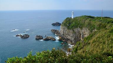 Paisagem costeira com um farol em um penhasco, afloramentos rochosos e o mar.