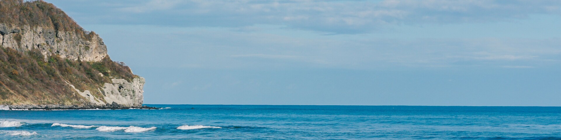 Una playa con olas, un acantilado y un cielo despejado.