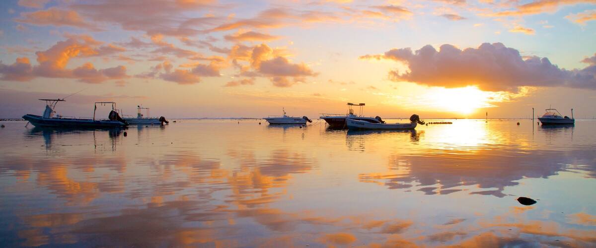 A calm lake at sunset with several boats anchored.
