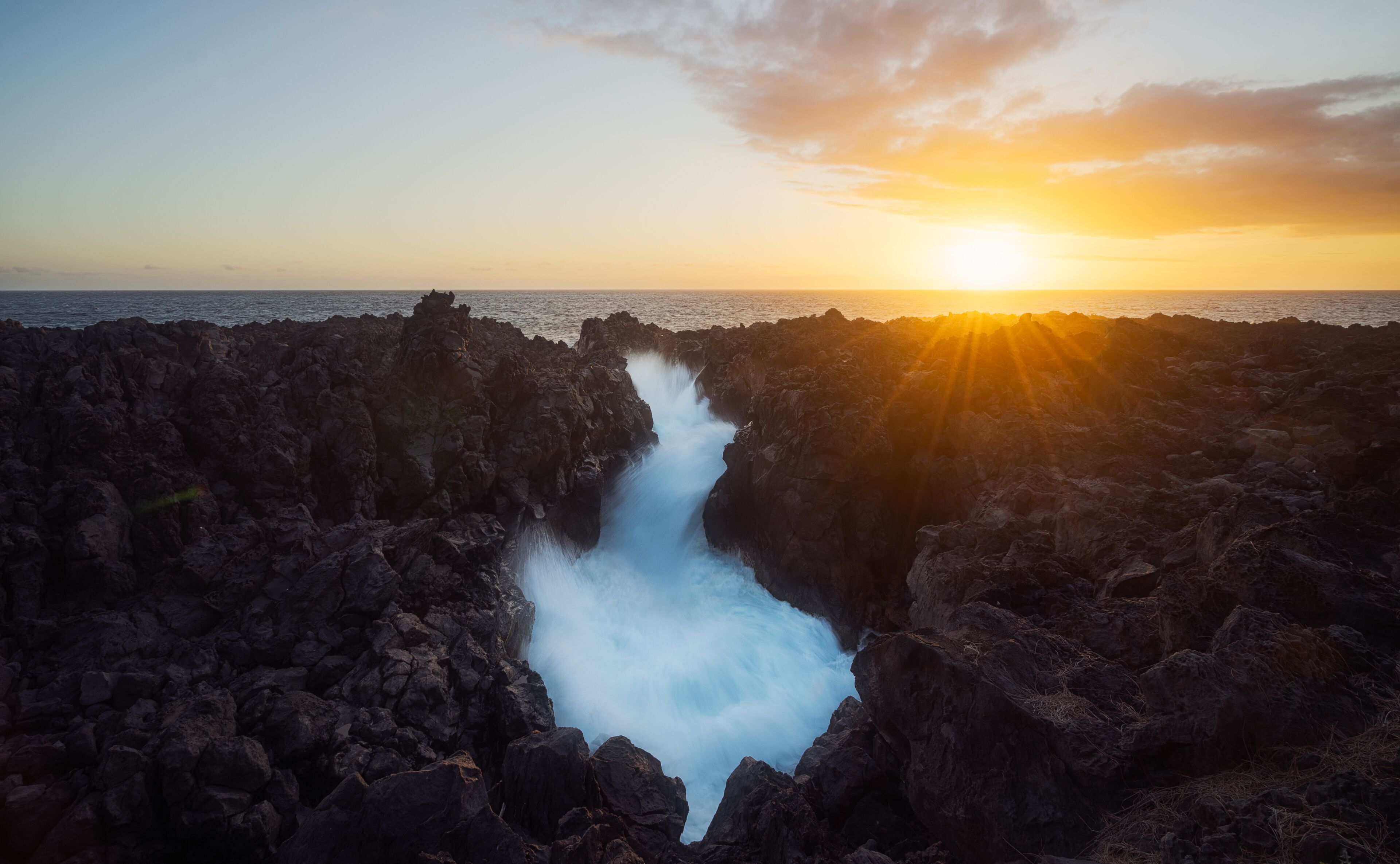 A coastal landscape with a waterfall flowing through a rocky gorge during sunset.