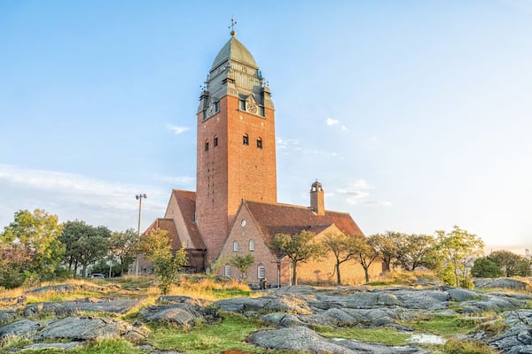 A historic church with a tall tower and a clock, surrounded by a rocky landscape and sparse trees.