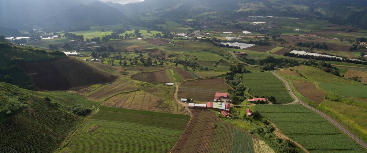 A rural landscape with terraced fields, a small village, and mountains in the background.