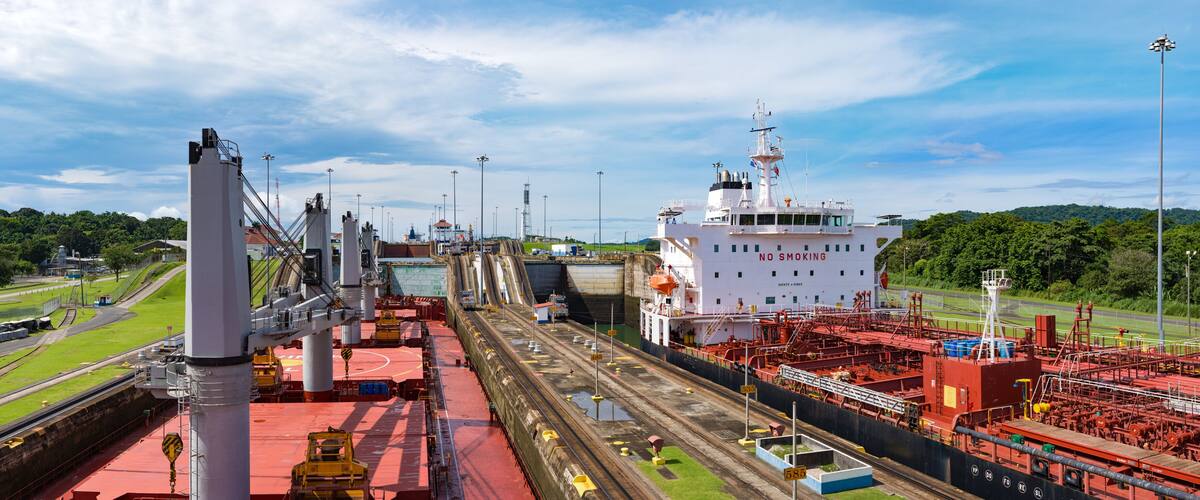 A large industrial port with a white ship docked, surrounded by cranes and rail tracks.