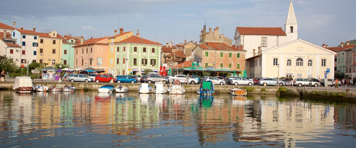 A waterfront with colorful buildings, a church, and parked cars along the canal.