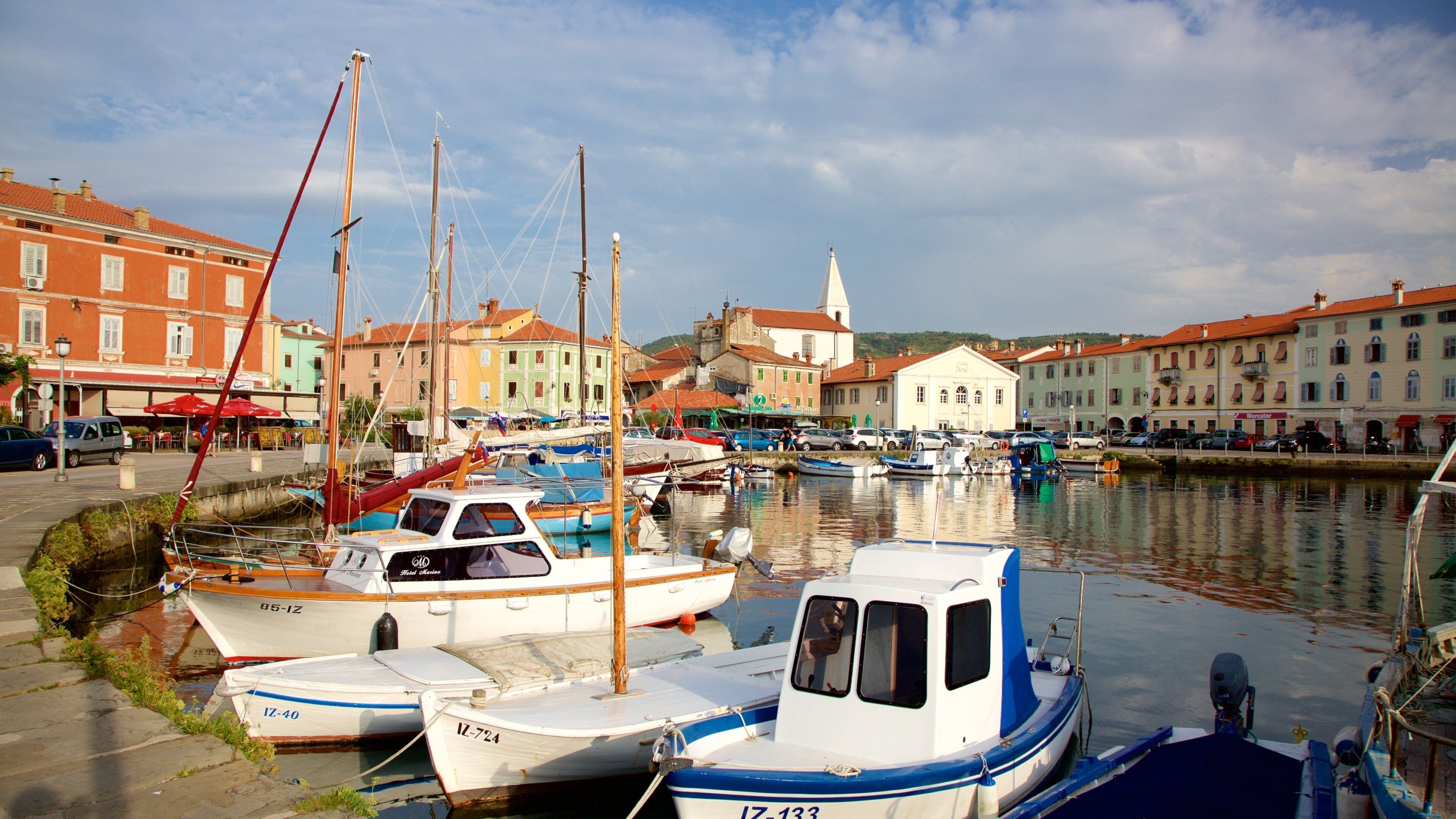 A marina with several boats docked, surrounded by colorful buildings and a church in the background.