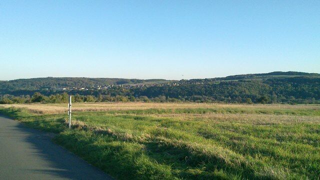 A rural road with a grassy field and a hill in the background.