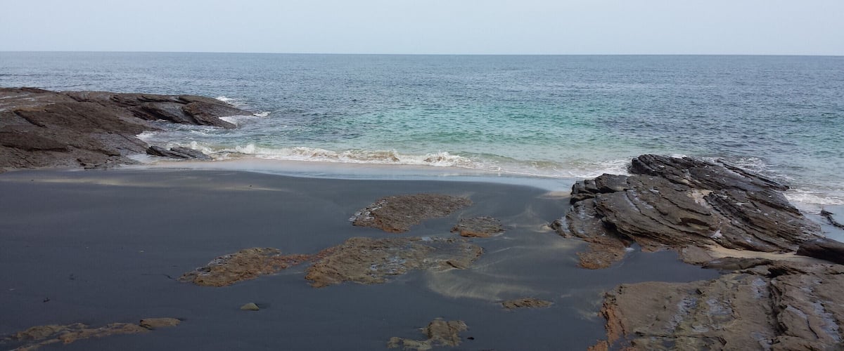 A rocky shoreline with clear blue water and a sandy beach.