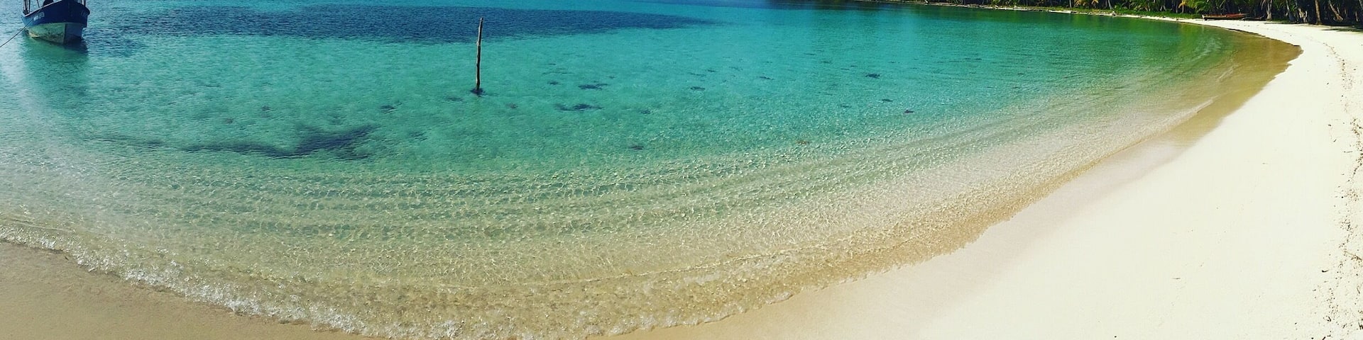 A beach with clear turquoise water, white sand, and palm trees.
