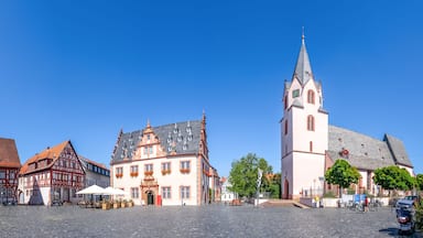 Uma praça de paralelepípedos com edifícios históricos, uma igreja com uma torre alta e bicicletas estacionadas perto.