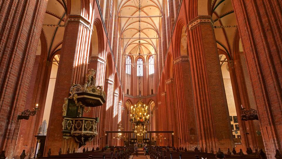 L’intérieur d’une cathédrale, avec de hauts plafonds en voûte, des murs en briques rouges et un grand lustre.