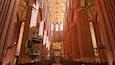 A cathedral interior with high vaulted ceilings, red brick walls, and a large chandelier.