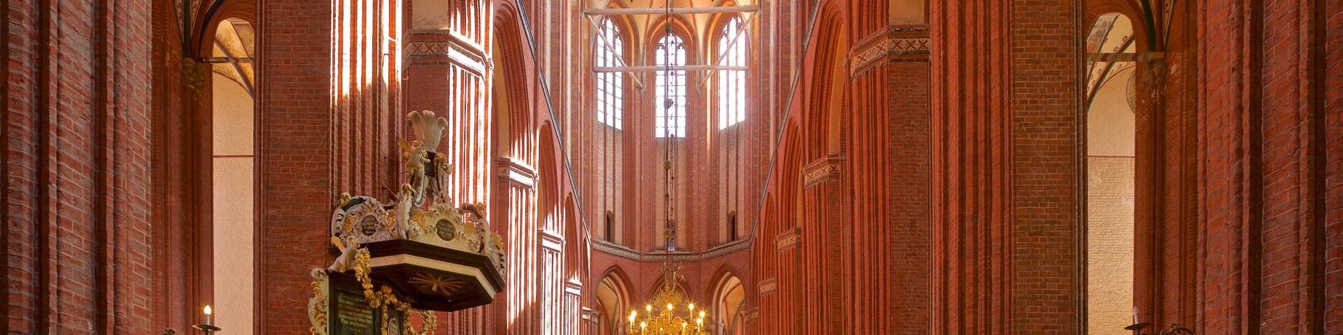 A church interior with high vaulted ceilings, a central aisle, and rows of wooden pews.