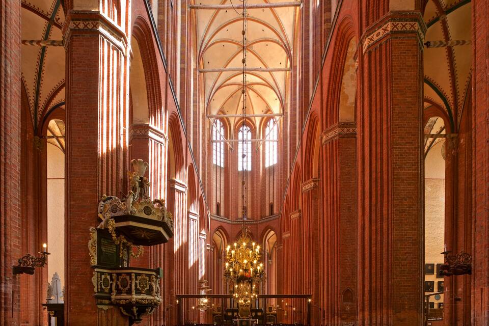 A Gothic-style cathedral interior with red brick walls, pointed arches, and a large chandelier.