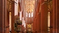A Gothic-style cathedral interior with red brick walls, pointed arches, and a large chandelier.