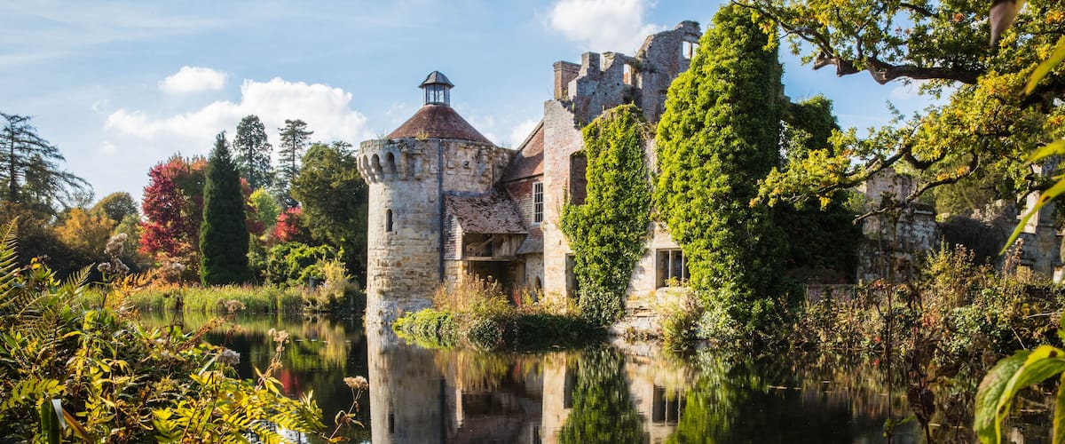 A historic castle with a moat, surrounded by lush greenery and a clear reflection in the water.