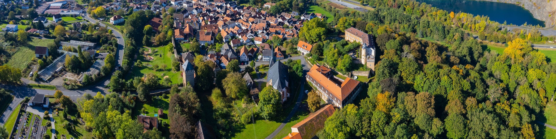 An aerial view of a town with a prominent castle, surrounded by lush greenery and a large lake.