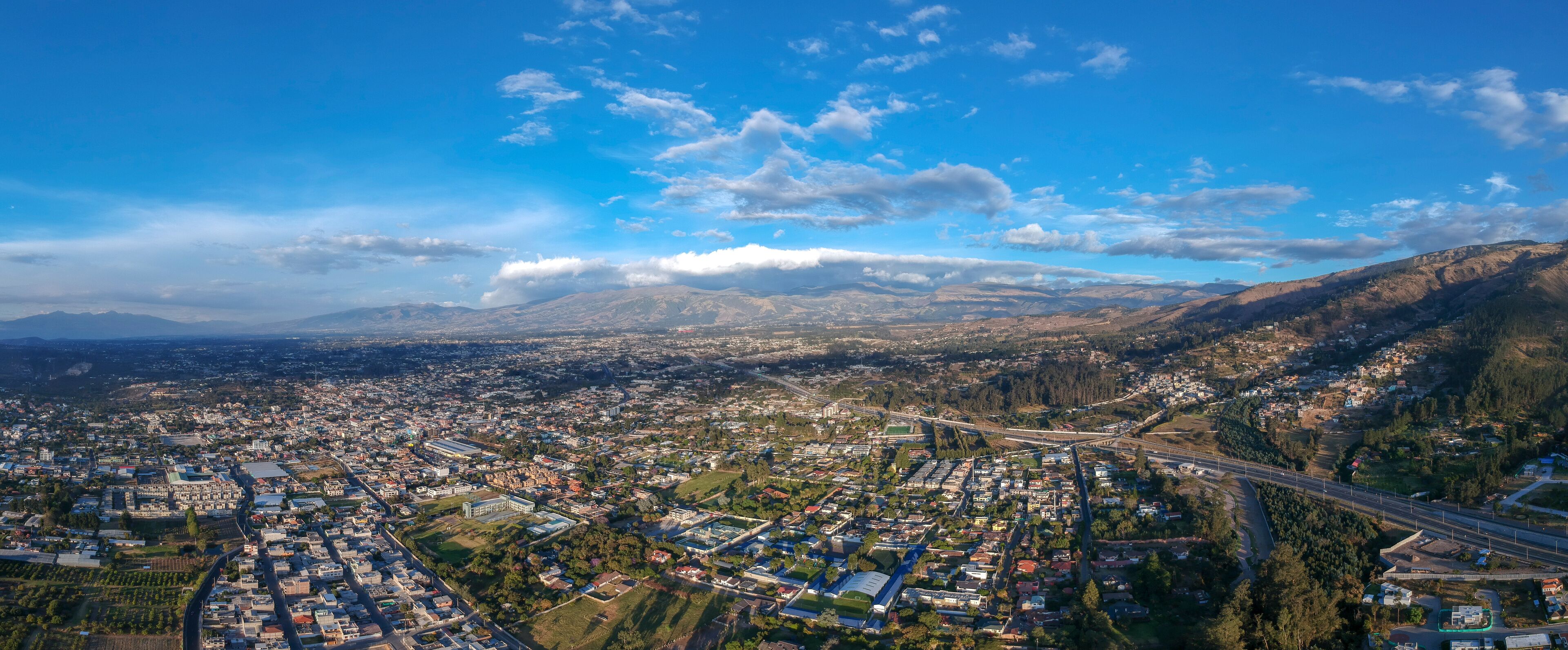 An aerial view of a city with a river, mountains, and a highway.