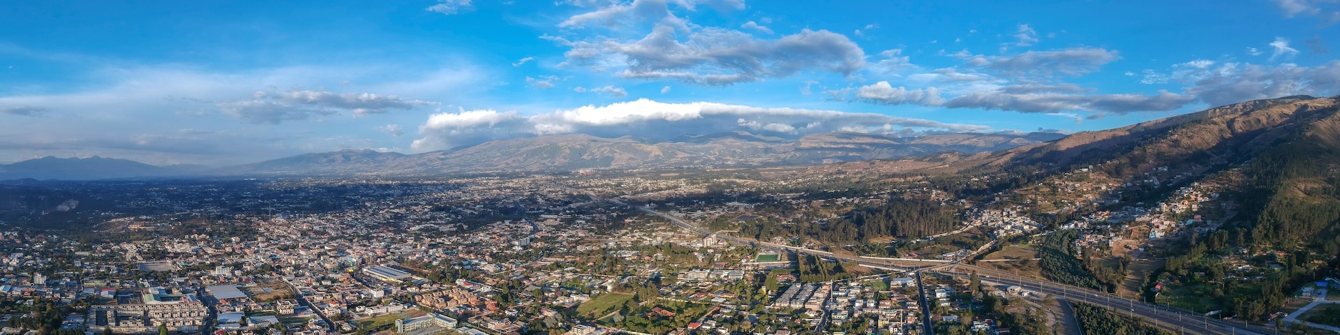An aerial view of a city with a river, mountains, and a highway.