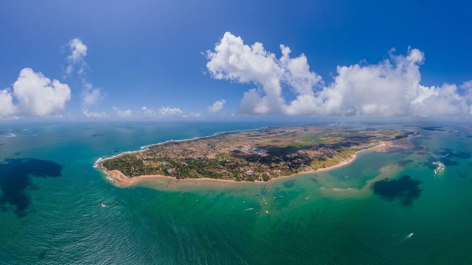 An aerial view of a tropical island with clear turquoise waters, a sandy beach, and scattered buildings.