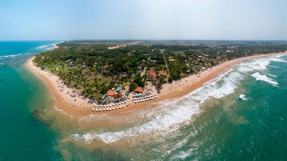 An aerial view of a tropical island with a beach, clear turquoise waters, and dense greenery.