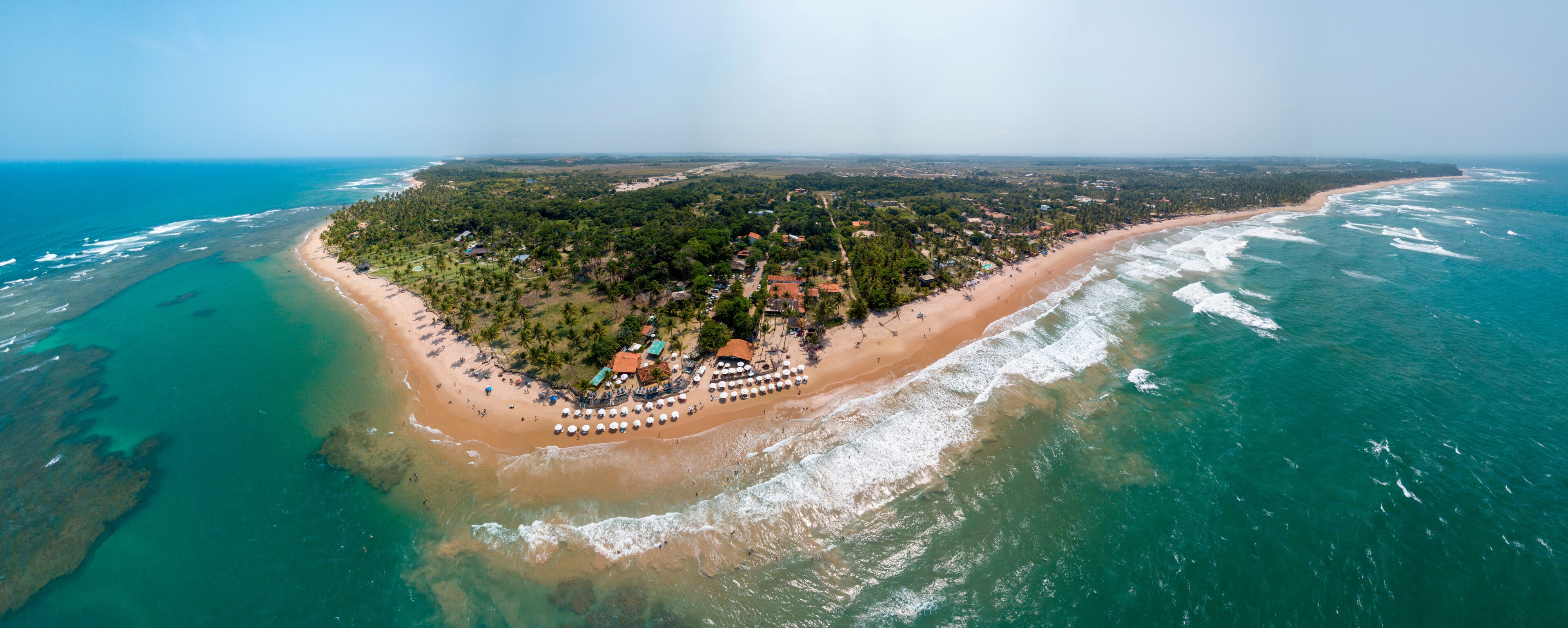 An aerial view of a tropical island with a beach, clear turquoise waters, and dense greenery.