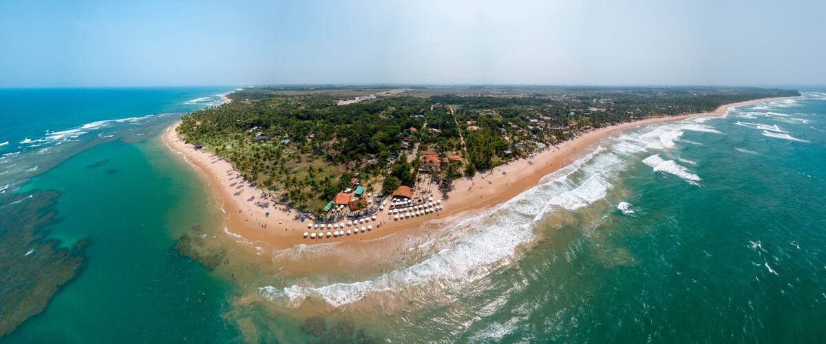 An aerial view of a tropical island with a beach, clear turquoise waters, and dense greenery.