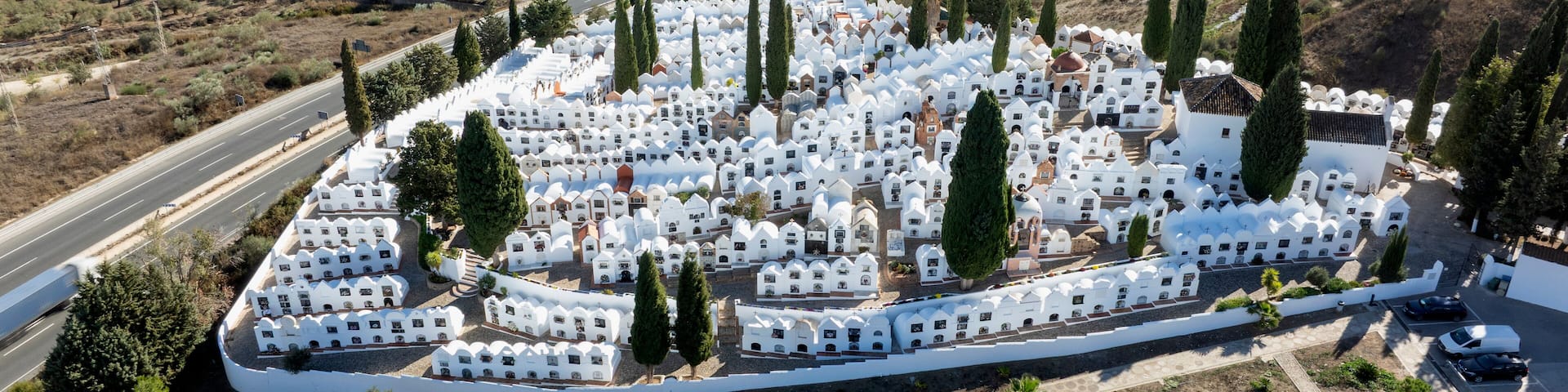 An aerial view of a cemetery with white tombs and cypress trees.