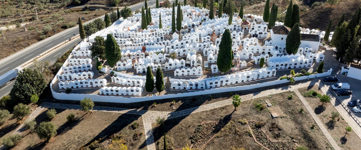 An aerial view of a cemetery with white tombs and cypress trees.
