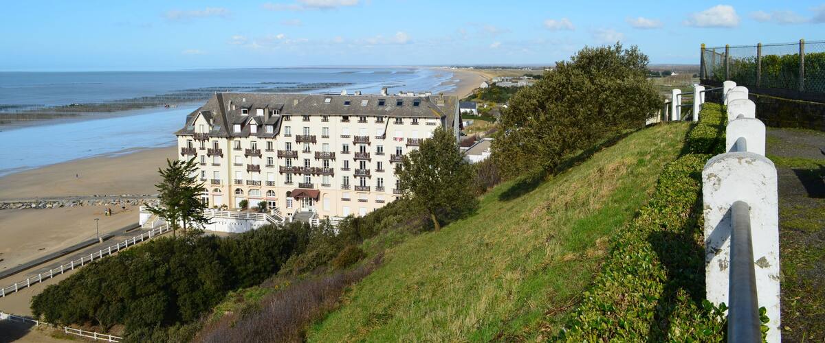 A coastal view with a large building overlooking the beach, a fence, and a clear sky.