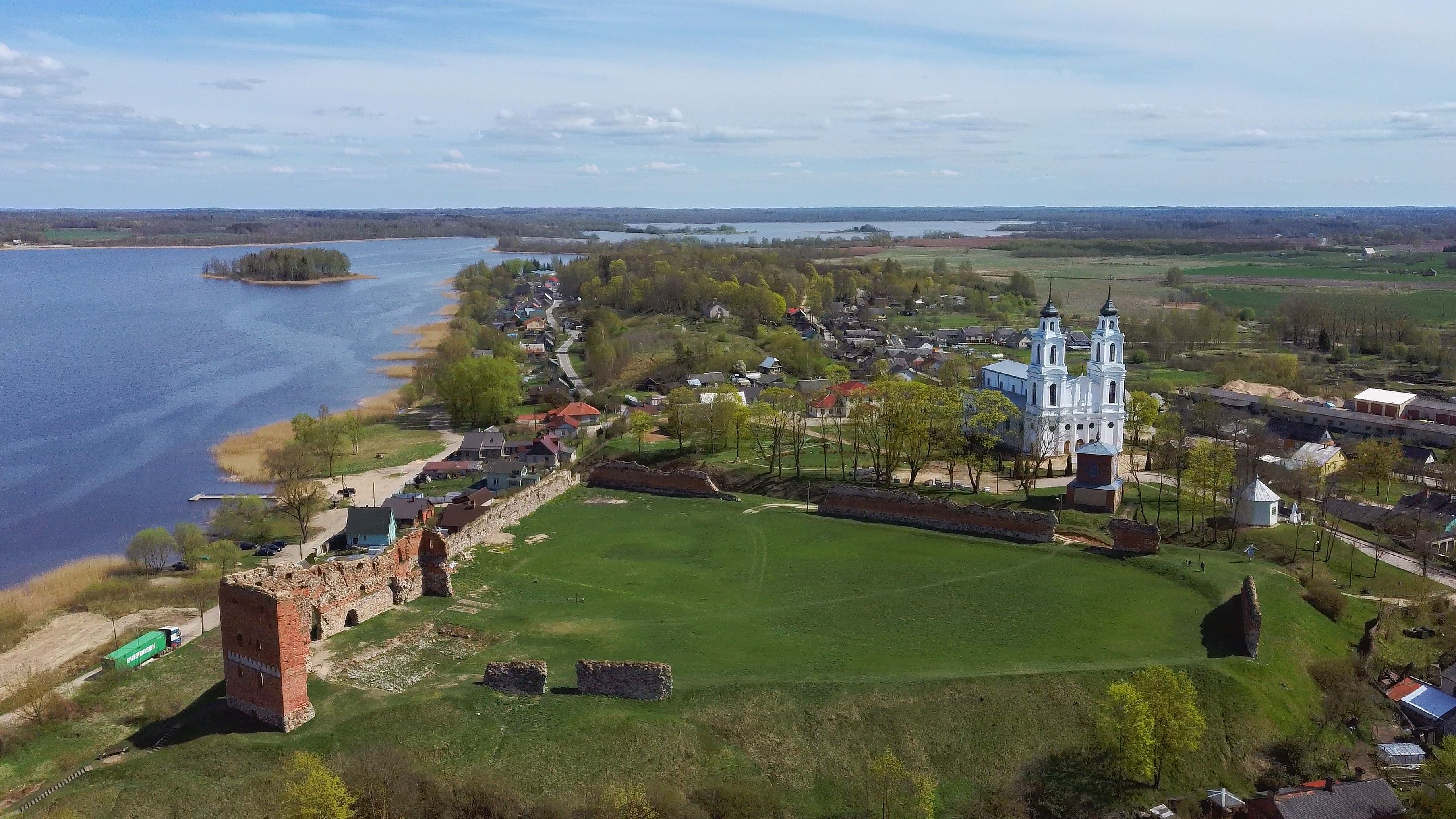 A riverside town with a prominent church, a large open field, and a historic brick structure.