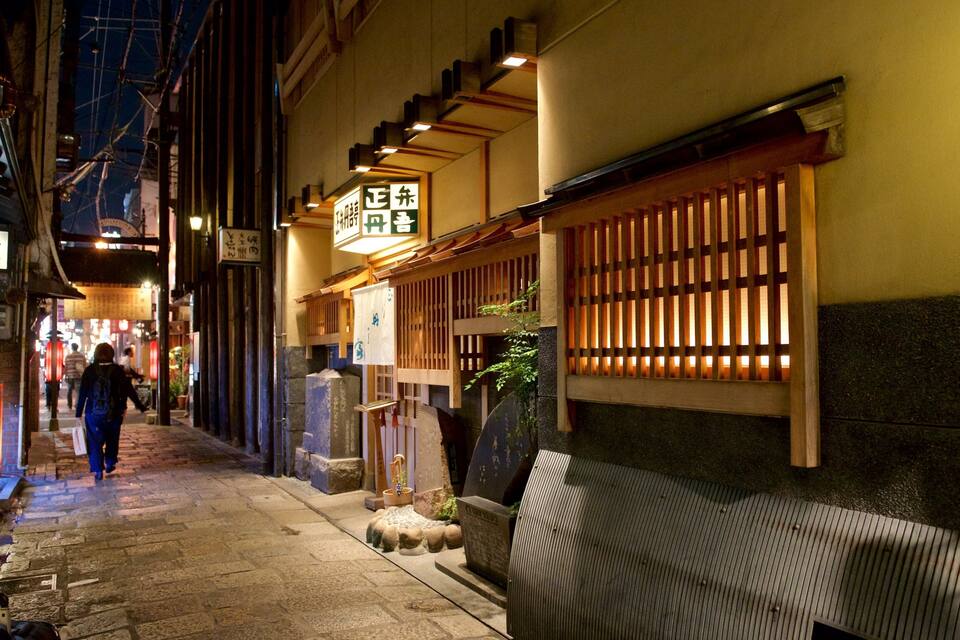 A narrow alleyway with traditional Japanese architecture, including wooden doors and signage with Japanese characters.