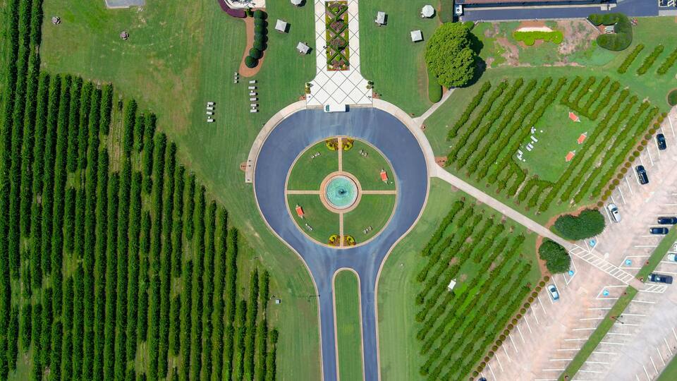 An aerial view of a roundabout with a central fountain, surrounded by landscaped areas and parking lots.