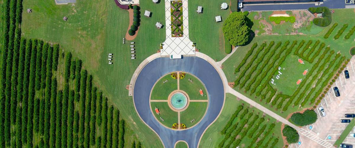 An aerial view of a roundabout with a central fountain, surrounded by landscaped areas and parking lots.