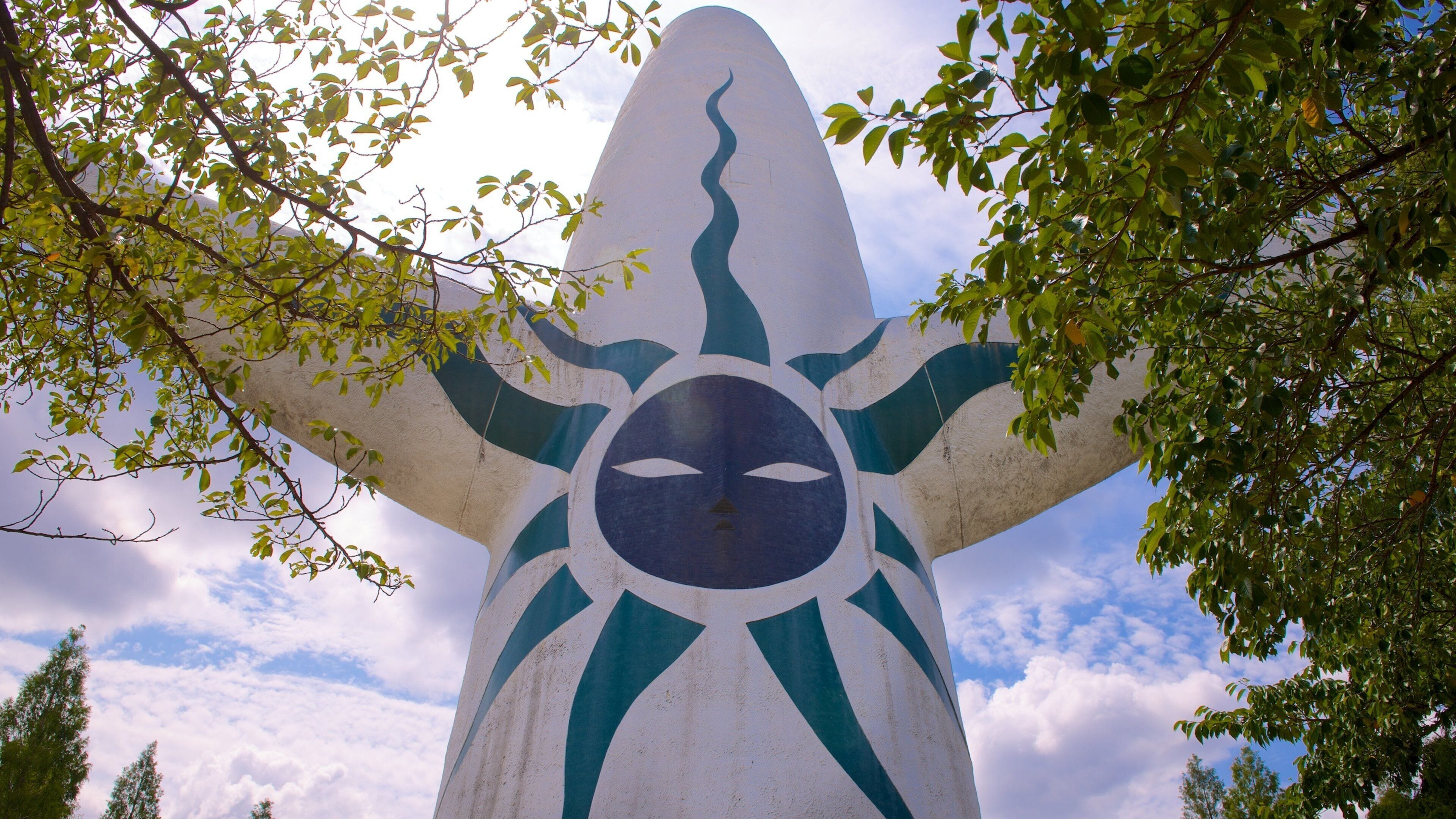 A large sculpture with a stylized face and arms, surrounded by trees.