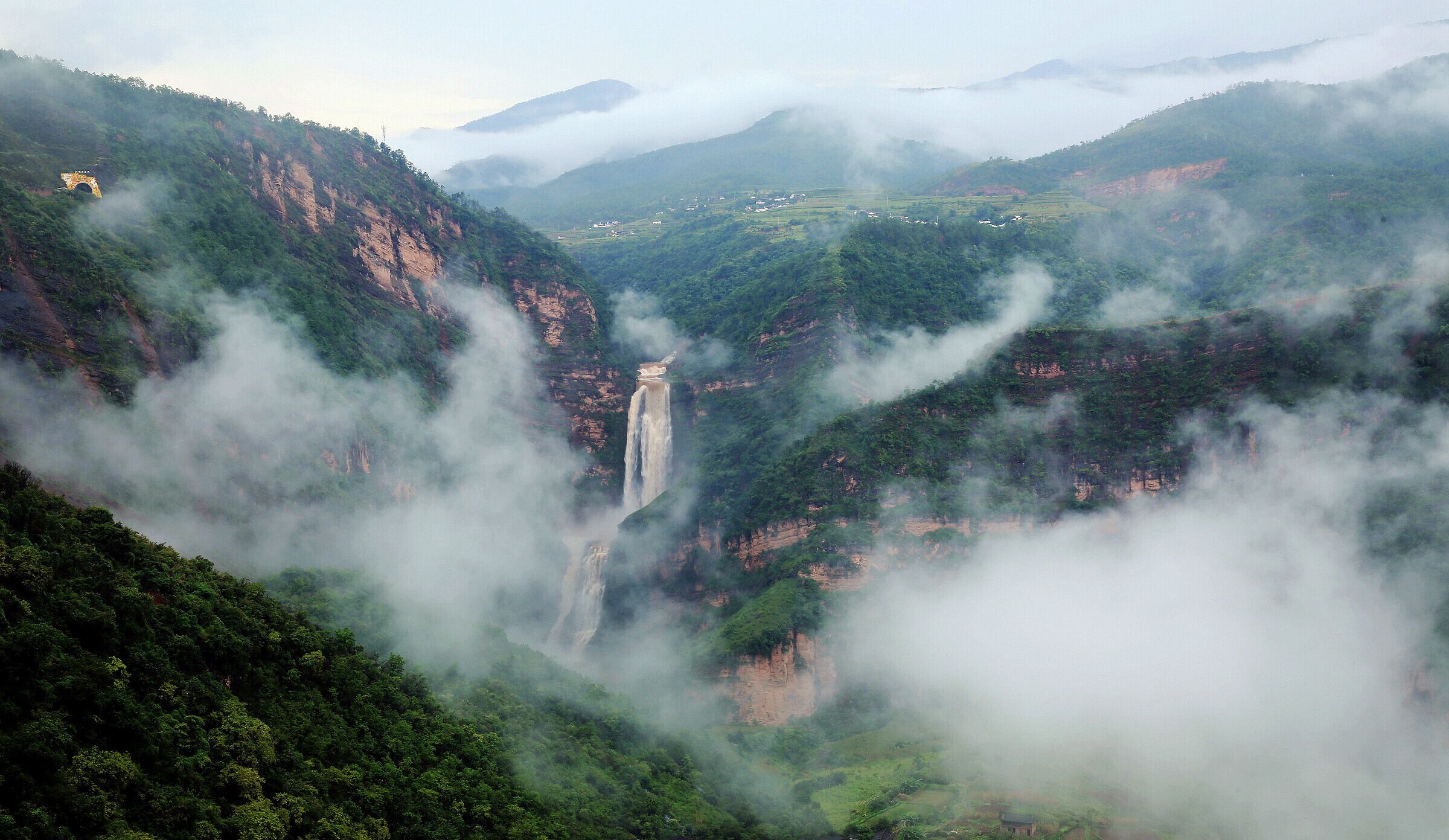 A misty valley with a waterfall and a small bridge.