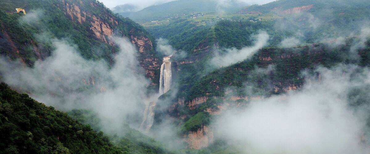 A misty valley with a waterfall and a small bridge.