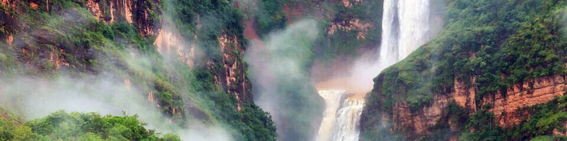Uma cascata em vários níveis, rodeada por vegetação exuberante e penhascos rochosos.