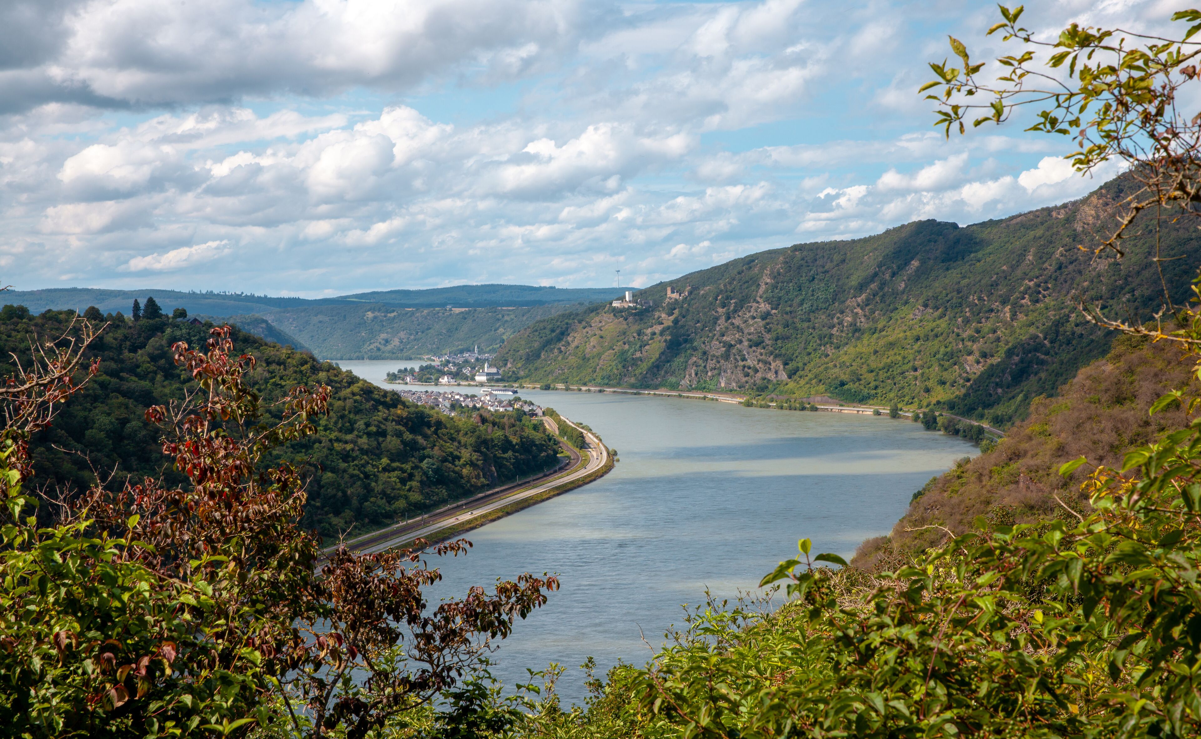 A river winding through a valley with hills on either side, a bridge crossing the river, and a distant castle-like structure.