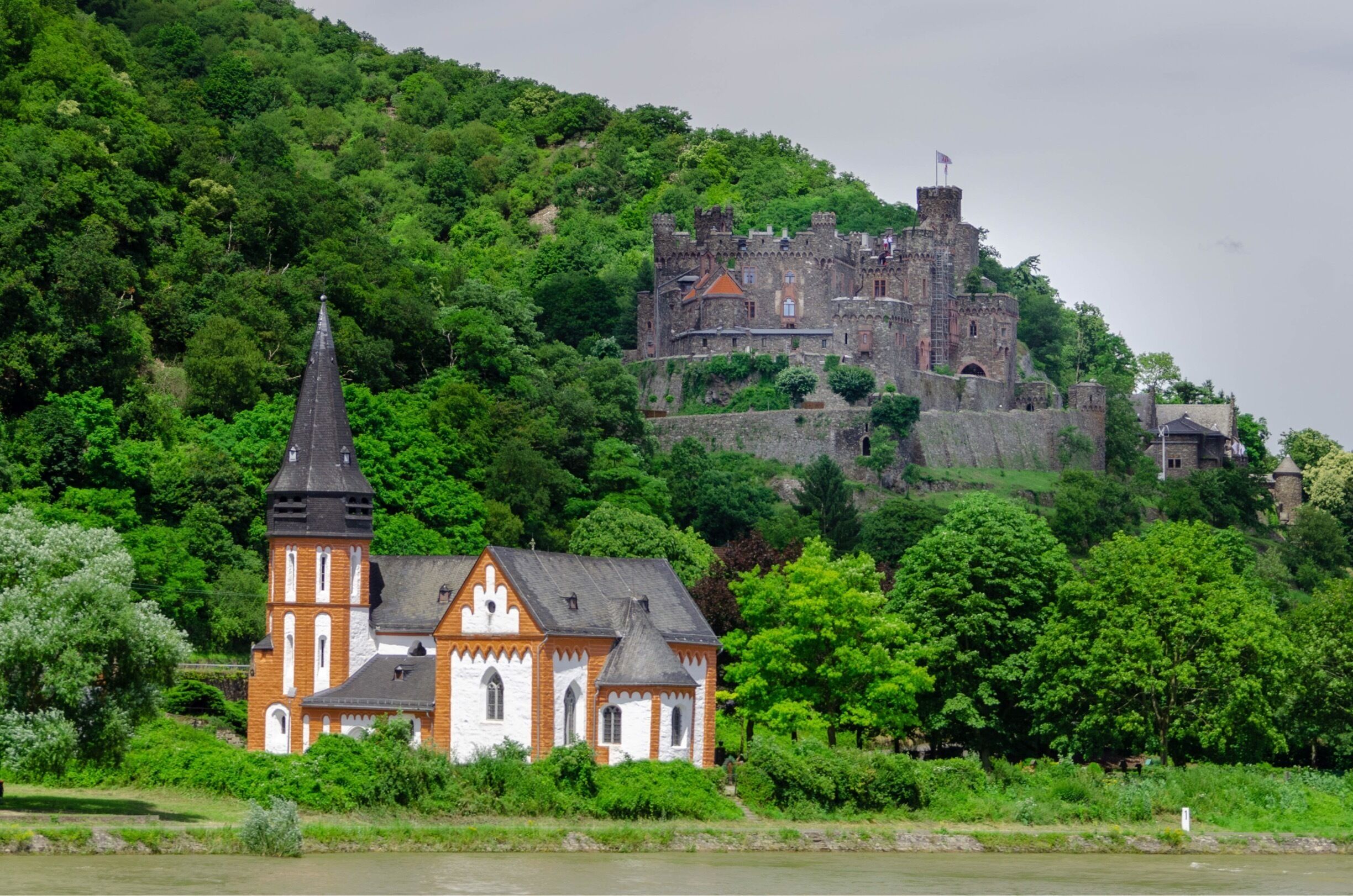 Sankt Clemens Kapelle in the foreground with Burg Reichenstein in the background, along Middle Rhine River in Germany.