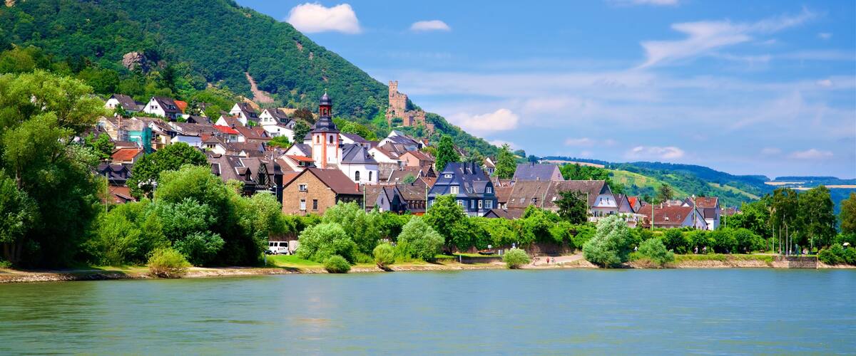 A riverside town with historic buildings, a church, and a castle on a hill.