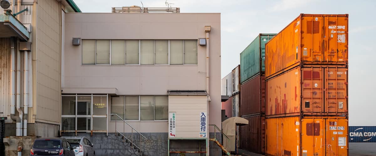 A building with a parking lot, stacked shipping containers, and a car.
